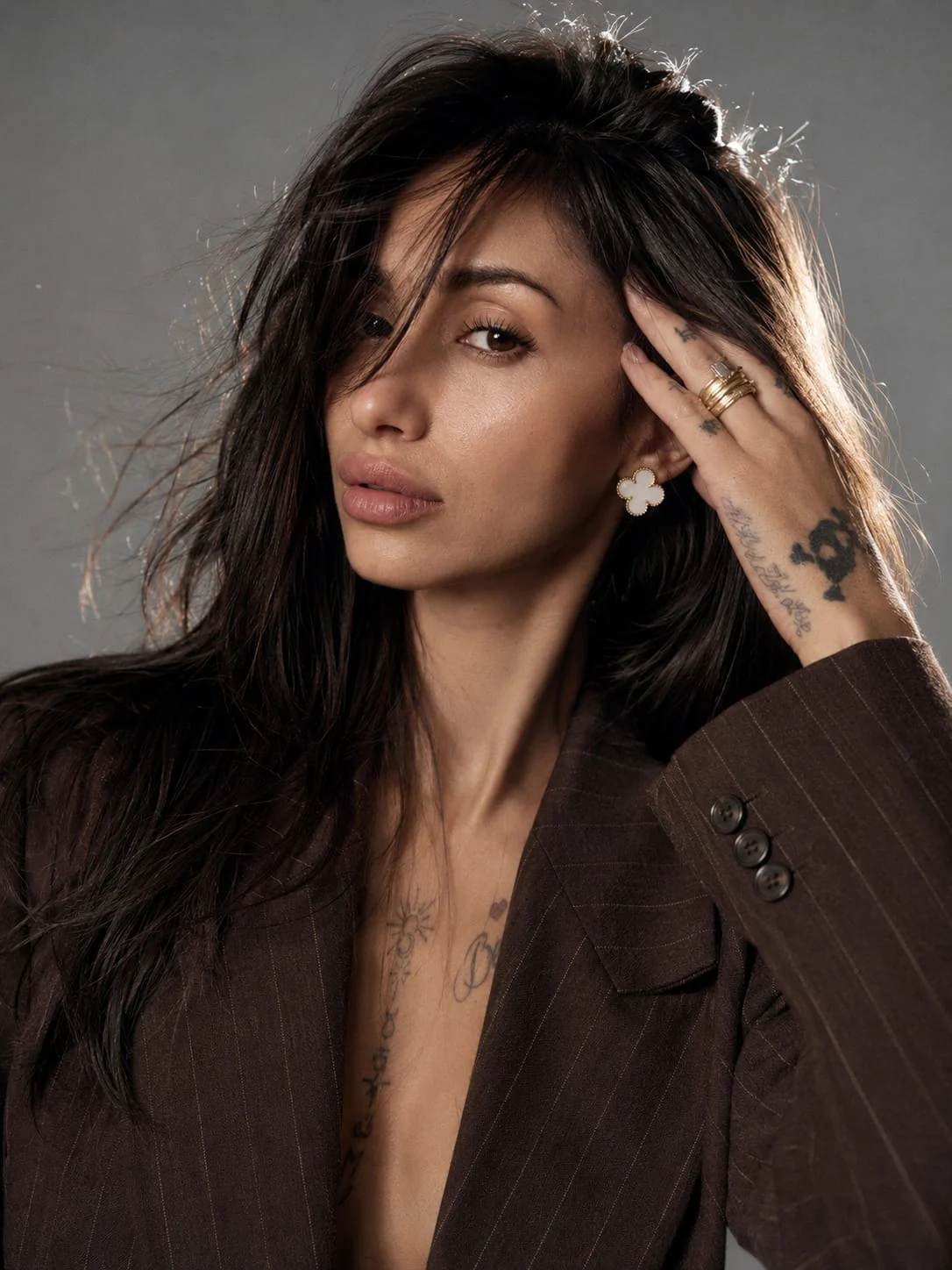 Portret de studio Aura în sacou maro cu dungi fine și cercei statement aurii.