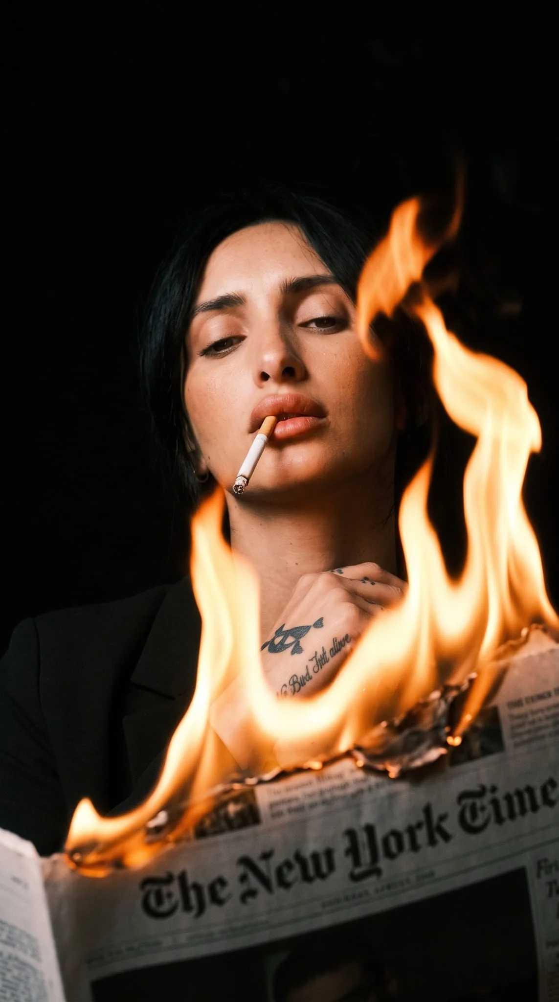 Portret editorial Aura în spatele unui ziar New York Times în flăcări, pe fundal negru.