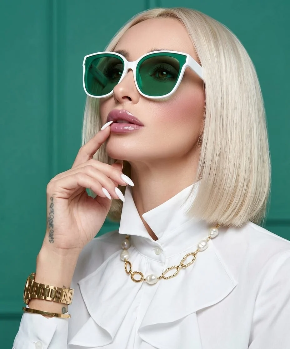 Portret fashion cu ochelari verde smarald, cămașă albă și bijuterii aurii cu perle.